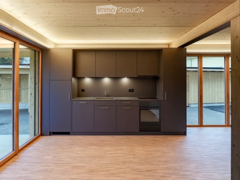 Modern kitchen with grey cabinetry, a sink, and a stove, featuring large windows and wooden flooring.