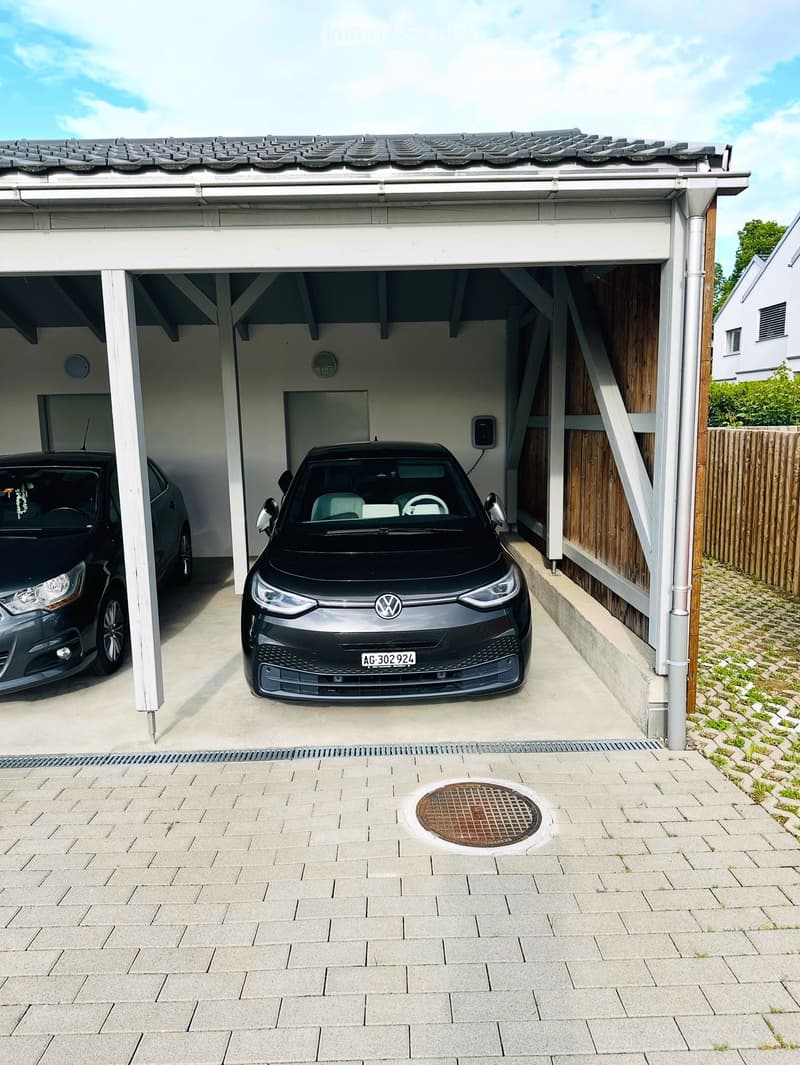 Attached garage with two cars parked inside, featuring a tiled roof and concrete floor.