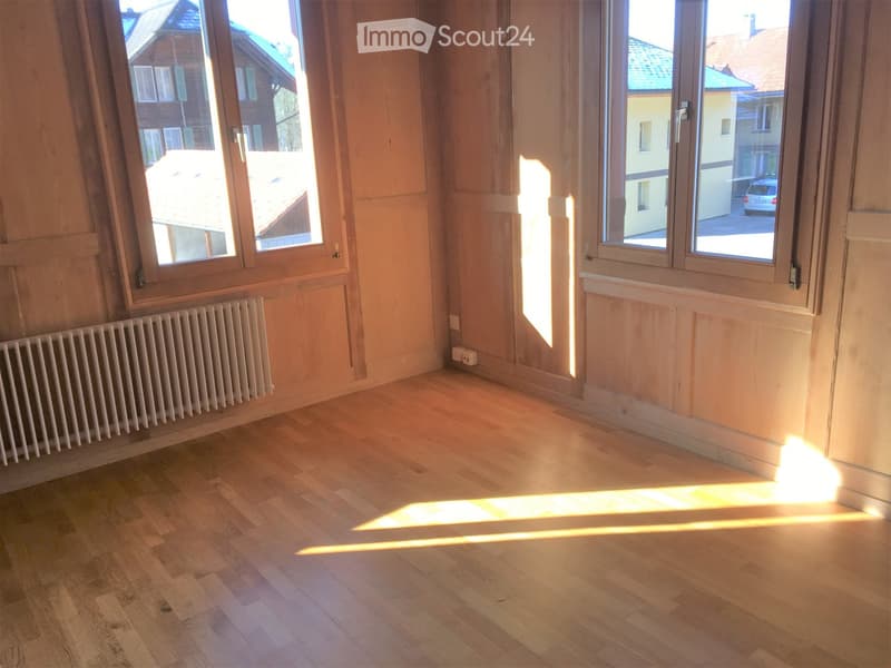 Empty room with wooden flooring, large windows, and a radiator on one wall.
