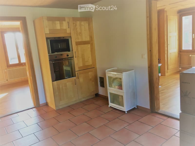 Bright kitchen with wooden cabinets, stainless steel oven and microwave, and a small white refrigerator. The floor is tiled in warm terracotta.