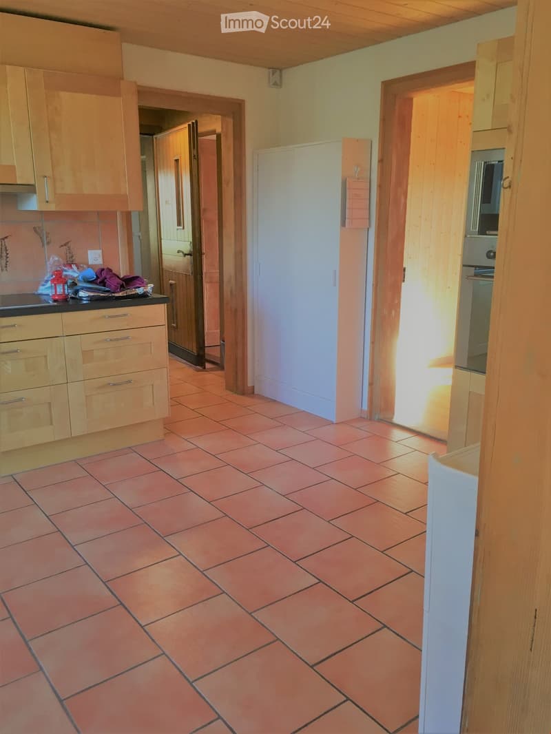 Bright kitchen with wooden cabinets, tiled floor, and a visible oven in the background.