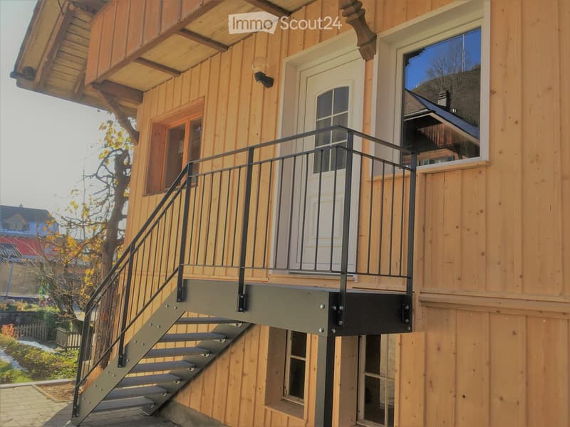 Wooden house exterior with a staircase leading to a balcony, featuring a white door and windows.