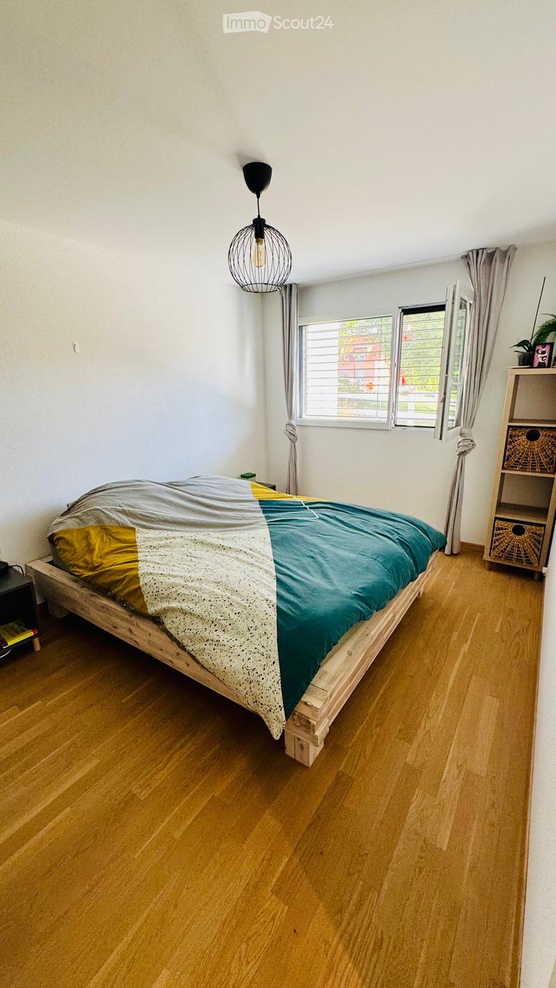 A modern bedroom with a wooden bed, colorful bedding, a pendant light, a nightstand, and a small shelf with baskets.