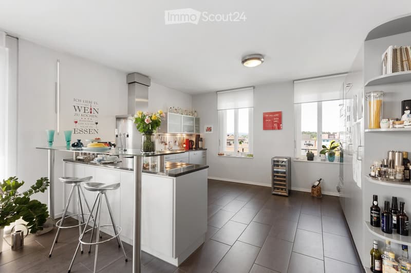 Modern kitchen with white cabinets, stainless steel appliances, a central island with bar stools, and a wine rack. The space features a sleek design with a vase of flowers on the island and various kitchen items neatly arranged.