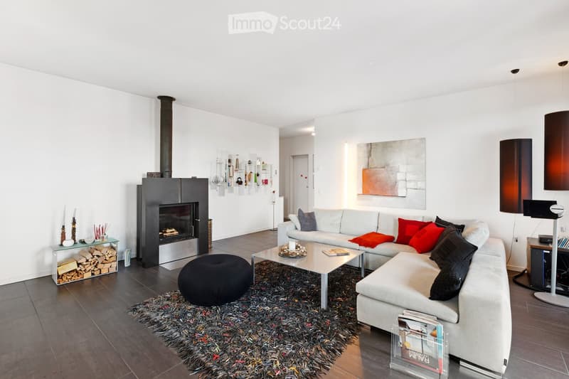 Modern living room with a white sofa, red and black cushions, a coffee table, a black ottoman, a fireplace, and a large abstract artwork on the wall.