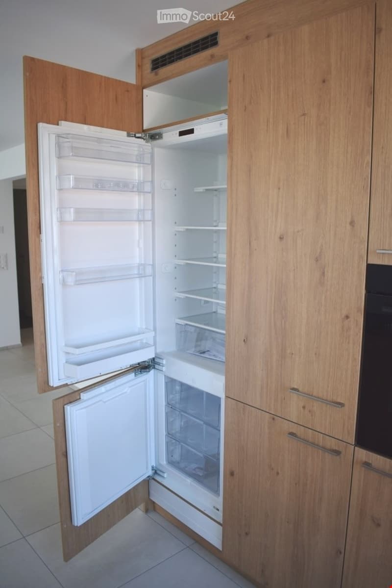 Modern kitchen with wooden cabinets and an open refrigerator, showing multiple shelves and drawers.