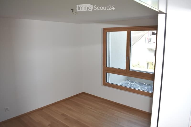 Empty room with light wooden flooring and white walls, featuring a large window with wooden frame and glass panes.