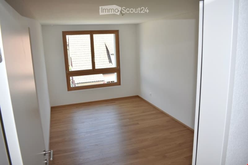 Empty room with wooden flooring and white walls, featuring a single window with wooden frame and glass panes.