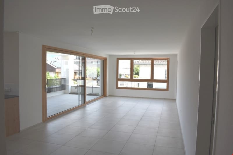 Empty room with tiled floor, large sliding glass door leading to a balcony, and a window with wooden frame. No furniture or equipment present.