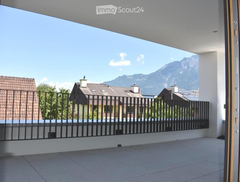 Balcony with a view of mountains, surrounded by a black metal fence, tiled floor, and open sliding door leading inside.