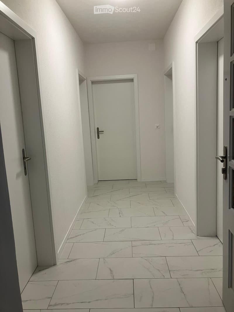 Clean, modern hallway with white walls, marble tiled floor, and several closed doors.