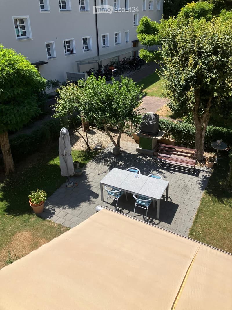 Courtyard with a table and chairs, benches, umbrella, potted plants, and a barbecue area.
