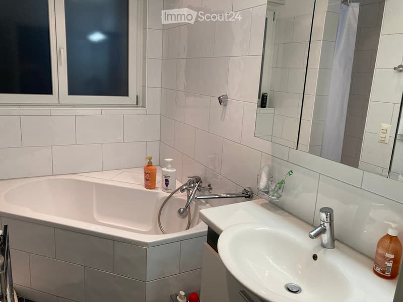 Modern bathroom with a bathtub, sink, mirror, and toiletries on the counter.