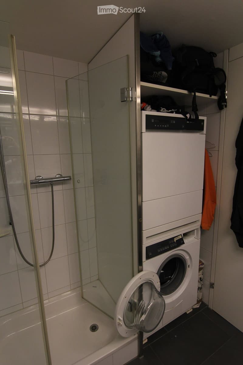 Modern bathroom with a shower cubicle, washing machine, and dishwasher above the washing machine, with shelves above.