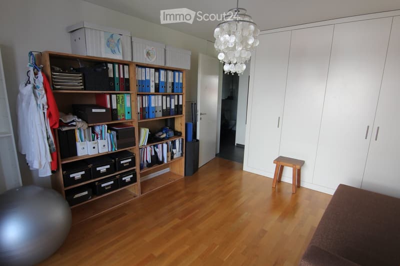 Wooden floor, built-in closet, desk with files and books, chandelier, exercise ball, small stool, sofa