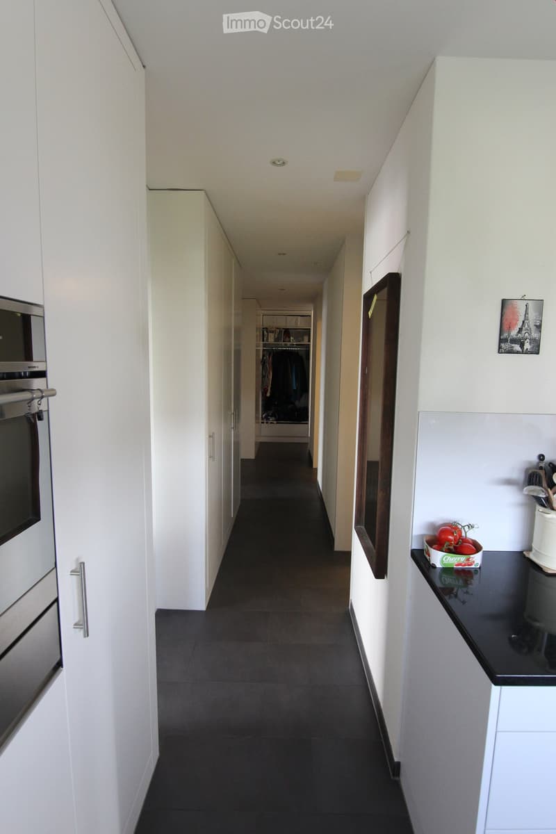 Long hallway with built-in white cabinets on either side, large open kitchen space at the end