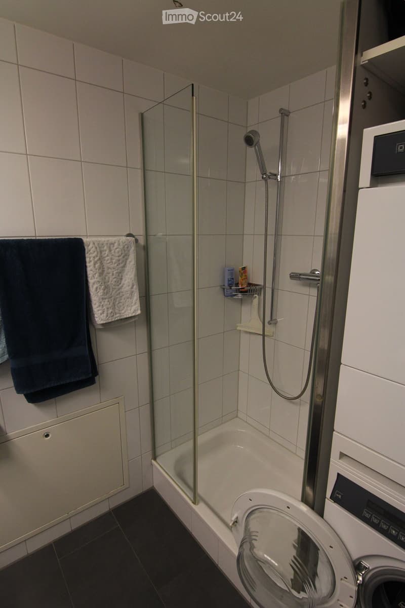 Small bathroom with shower cubicle, white tiles, white washing machine, towels, white shower curtain
