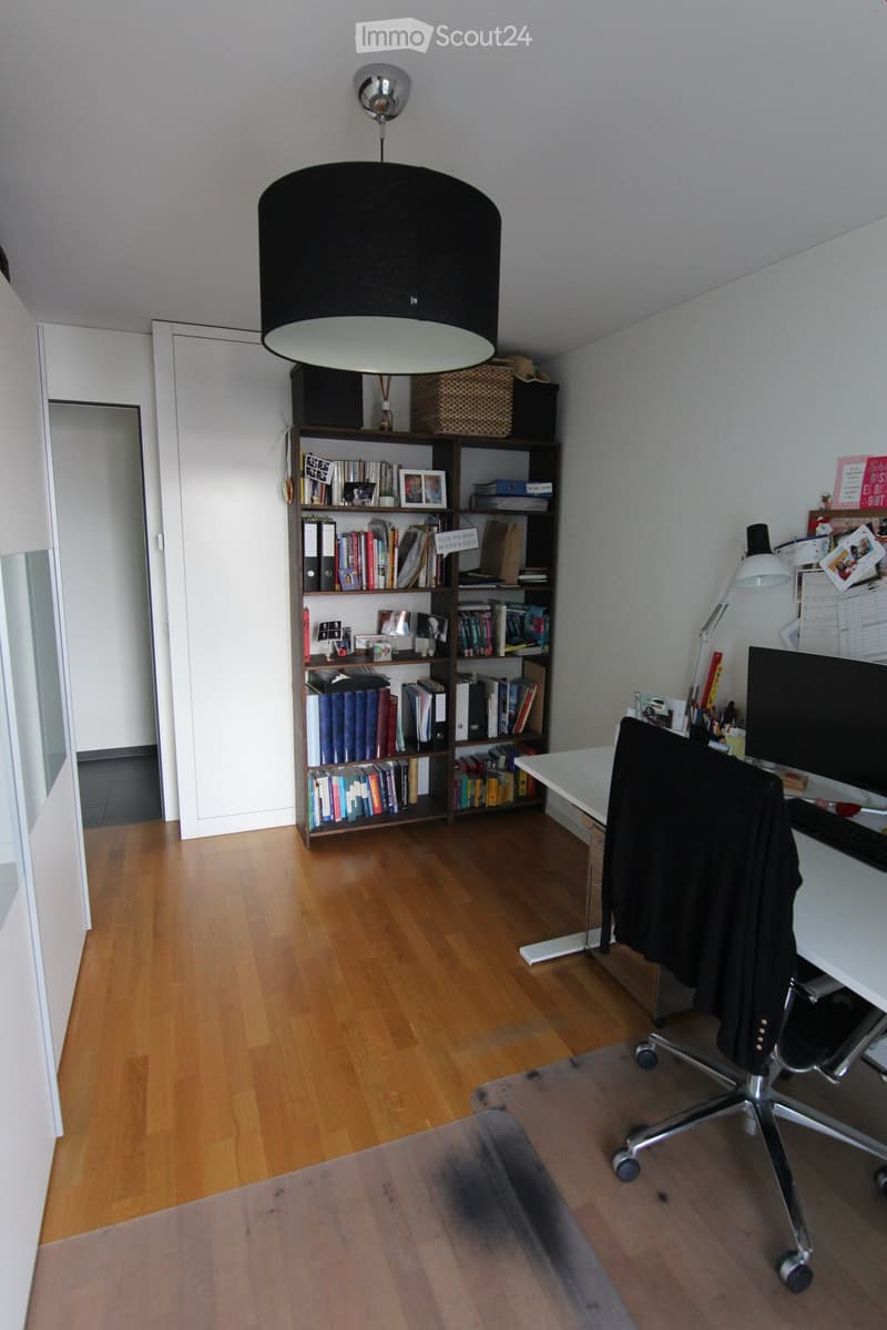 Office desk with computer, chair, bookshelf with many books, lamp, ceiling lamp