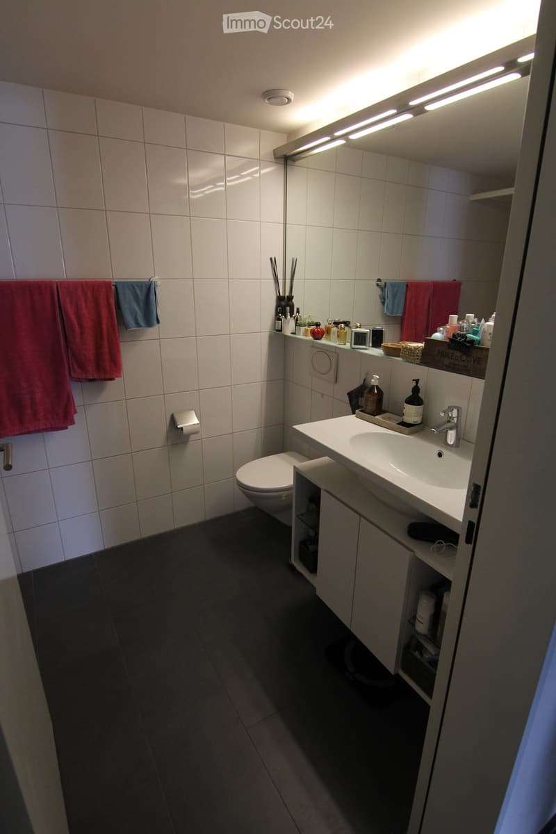 a bathroom with white tiles, a white sink, a toilet, and towels on the wall