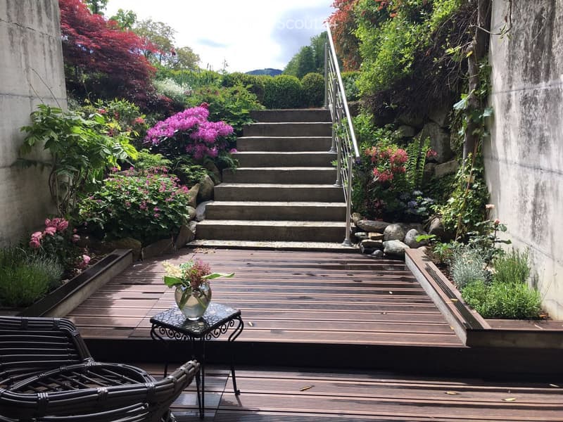 wooden deck, steps leading up, surrounded by gardens, table with plant