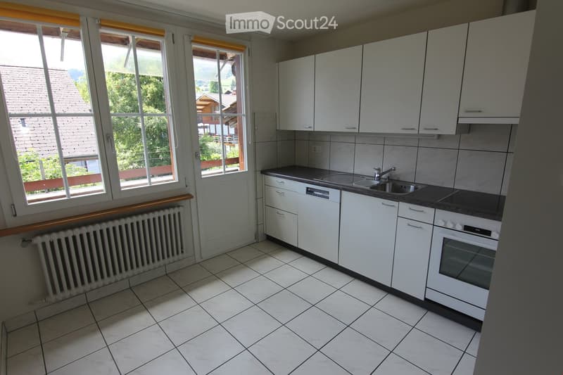 Modern kitchen with white cabinets, tiled floor, sink, oven, dishwasher, and large windows overlooking a scenic outdoor area.