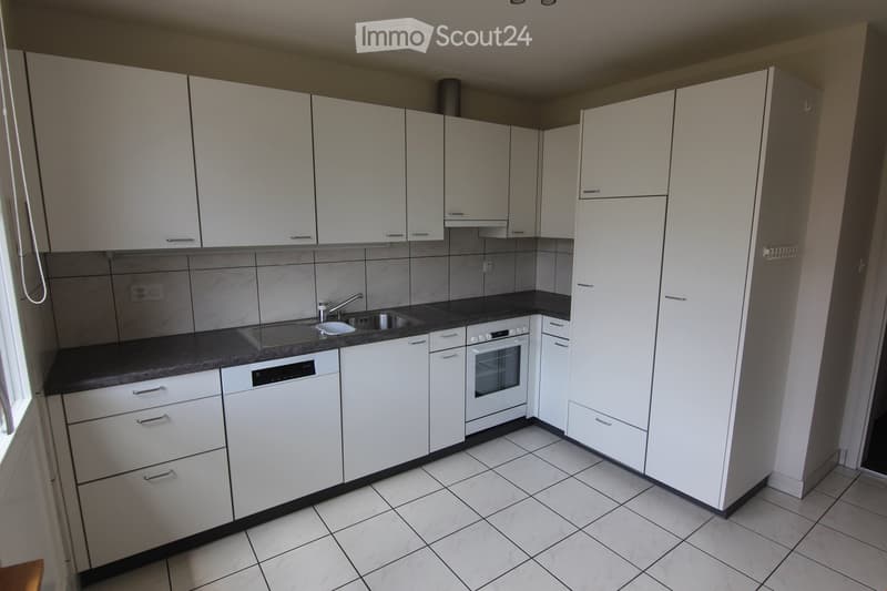 Modern kitchen with white cabinets, dark countertops, tiled floor, and built-in appliances including an oven and dishwasher.