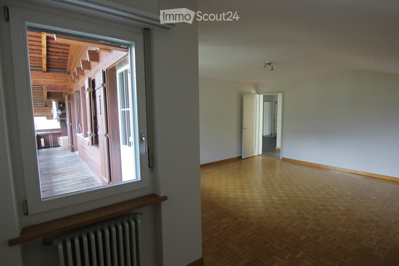 Empty room with wooden flooring, white walls, and a large window opening to a wooden deck area. No furniture or personal items are present.