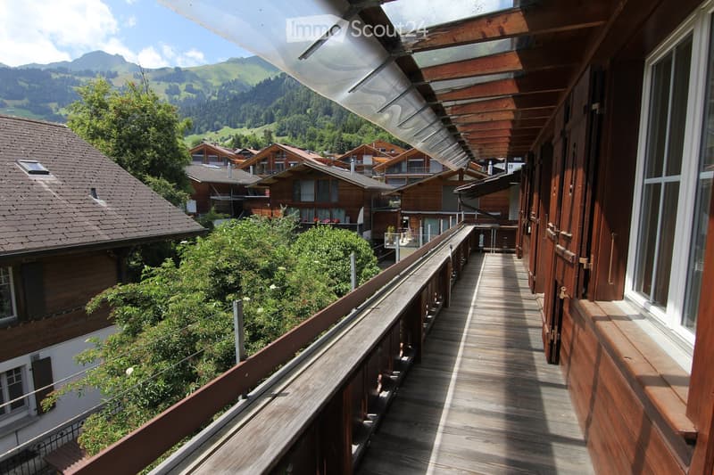Wooden balcony overlooking a scenic mountain valley with traditional wooden houses and lush greenery.
