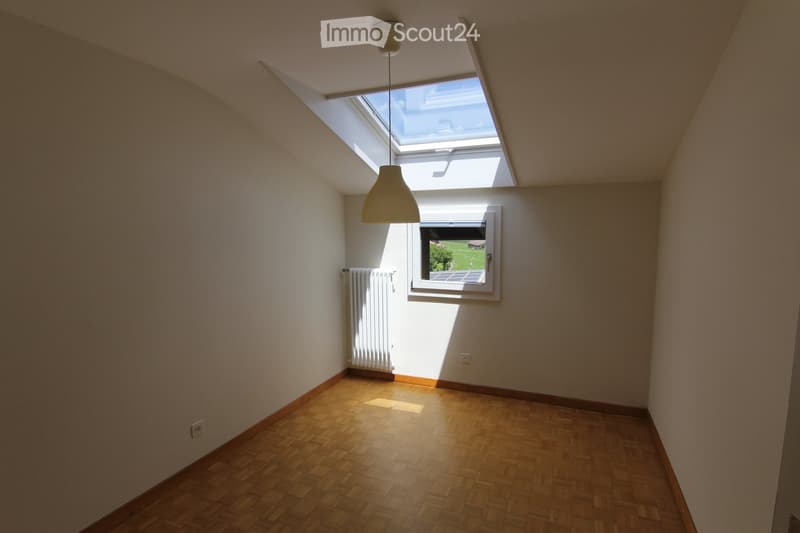 Empty room with wooden flooring, white walls, a skylight window, a side window, a radiator, and a hanging light fixture.