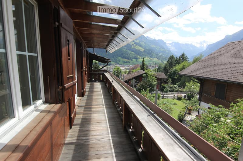 Wooden balcony with a railing, overlooking a scenic valley and mountains.