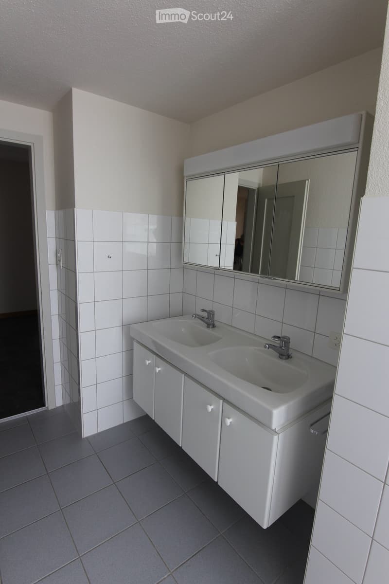 Modern bathroom with white tiled walls, grey tiled floor, double sink, mirrored cabinet, and white cabinetry.