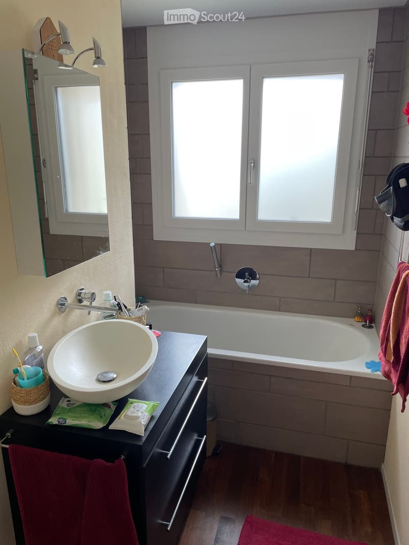 Modern bathroom with a white sink, bathtub, and large mirror. Includes a towel rack, toiletries, and a window for natural light.