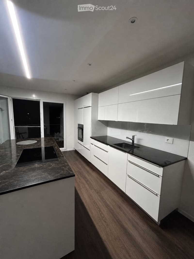 Modern kitchen with white cabinets, black countertops, and wooden flooring. Features include an oven, sink, and faucet.