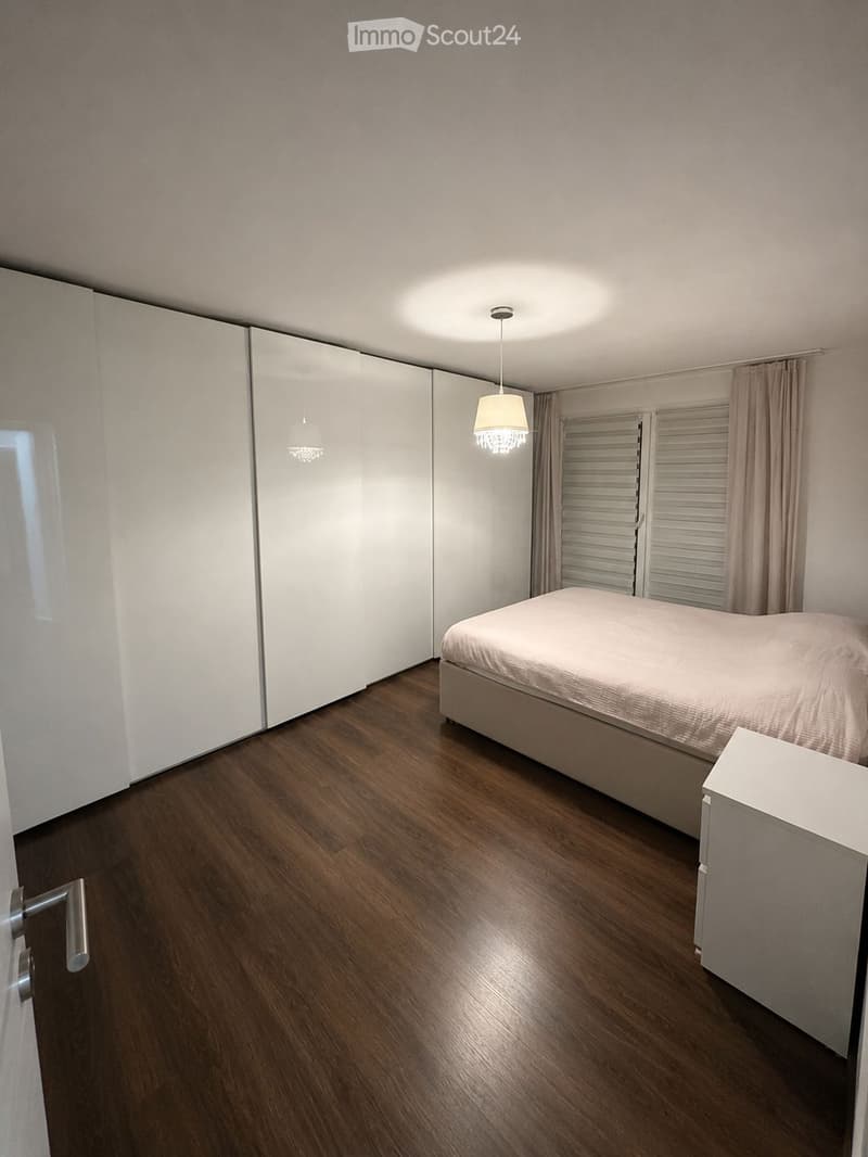 Modern bedroom with wooden flooring, a neatly made bed, built-in white wardrobe, and a small nightstand.