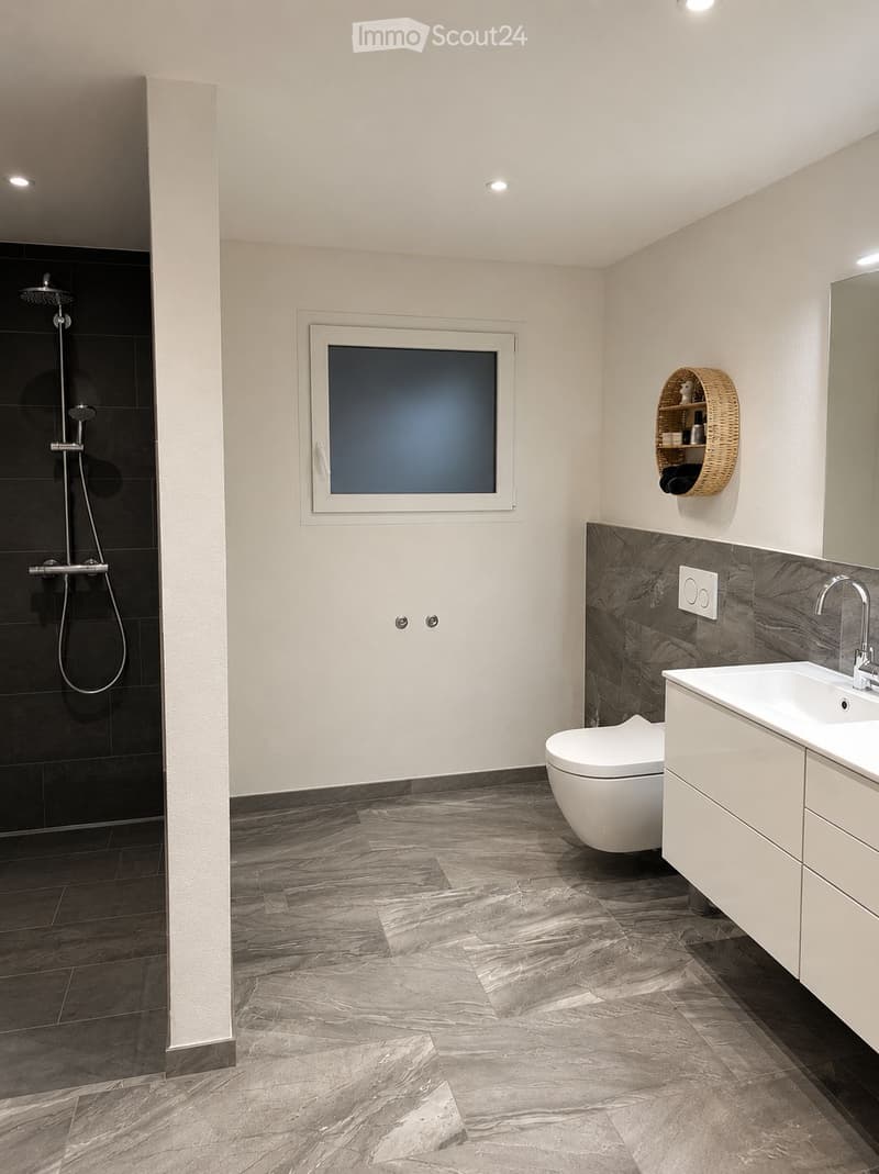 Modern bathroom with marble flooring, white walls, a toilet, sink, shower, and a wicker basket on the wall.