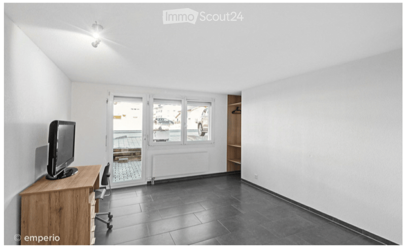 Bright room with wooden desk, chair, and screen, large windows with view of outdoor area, dark tiled floor.