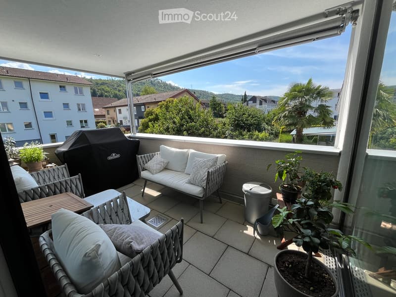 Balcony with a sofa, chairs, a small table, a covered grill, and potted plants, offering a scenic view of the surrounding area.