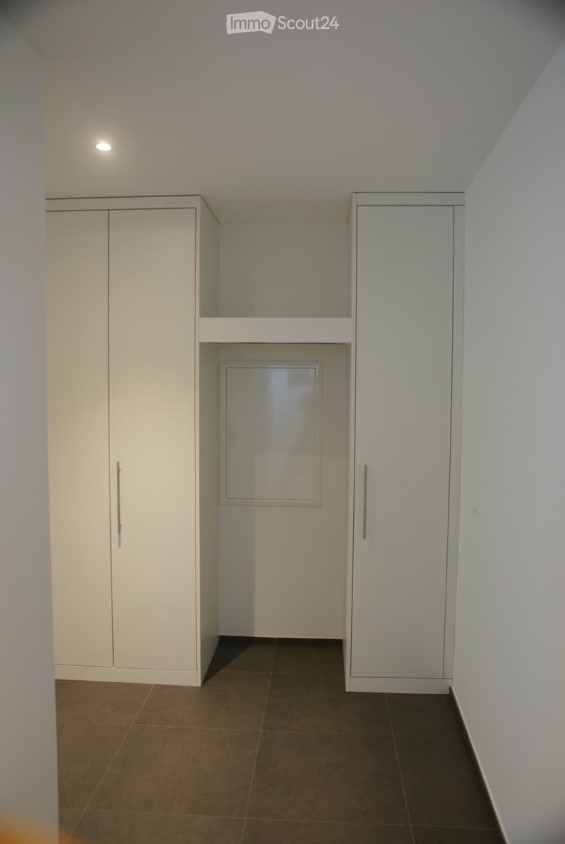 Empty hallway with white walls, dark tiled floor, and built-in white cabinets with mirrored doors.
