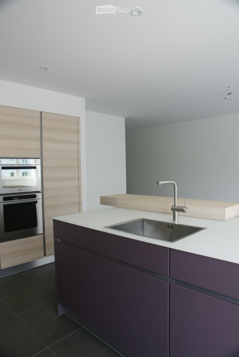 Modern kitchen with white countertops, dark purple cabinets, stainless steel sink, and built-in oven.