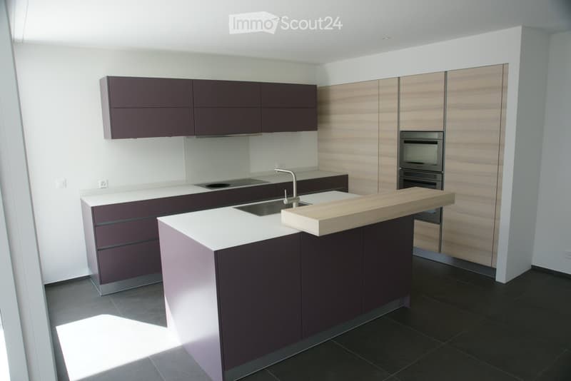 Modern kitchen with dark brown cabinets, white countertops, a central island, and built-in appliances including a sink and oven.