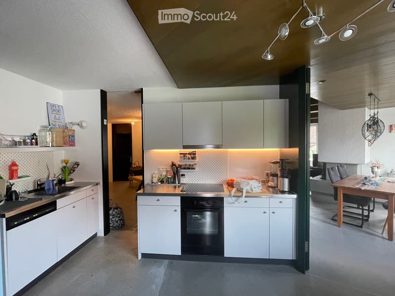 Modern kitchen with white cabinets, stainless steel appliances, and a central island. The space features a sink, oven, blender, and a small dining area with a table and chairs.