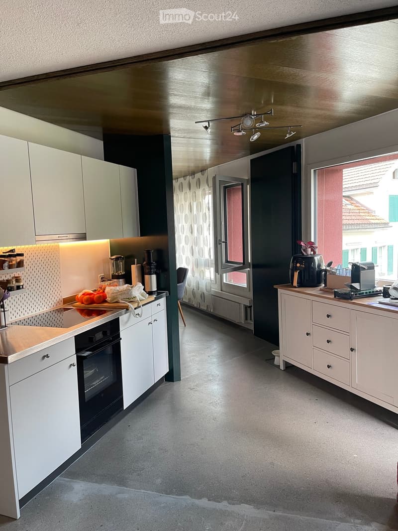 Modern kitchen with white cabinets, stainless steel appliances, and a large window overlooking the street.