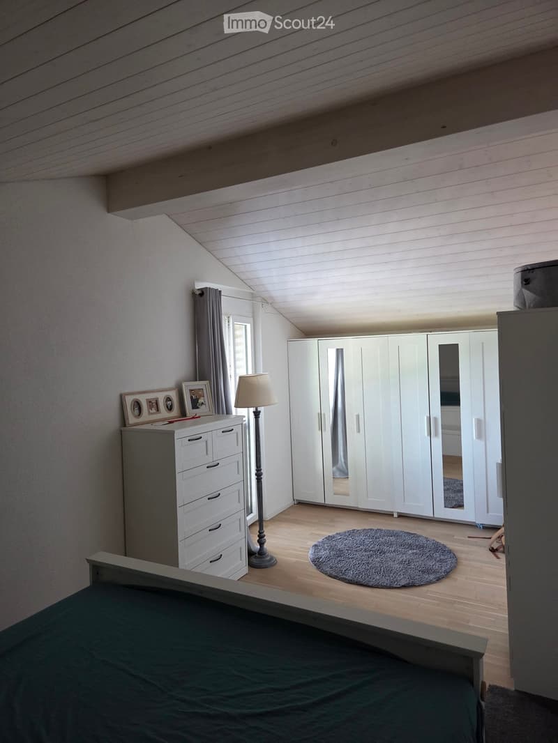 Cozy attic bedroom with wooden floors, slanted ceilings, large wardrobe, dresser, floor lamp, and round rug.