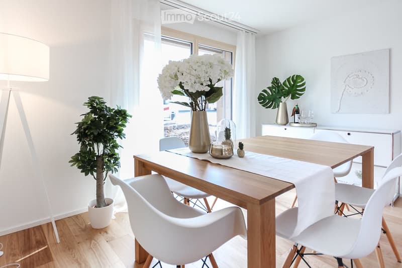 Dining room with wooden table, white chairs, white curtains, white flowers in vase, potted plants, white lamp, white cabinet, white artwork