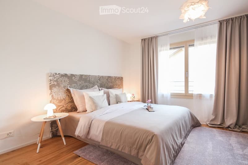 A bedroom with a bed, nightstand, and a window with curtains