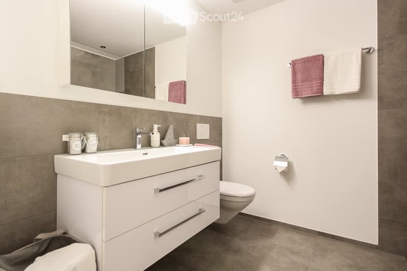 Bathroom with white sink, mirror, toilet, and towel rack with towels