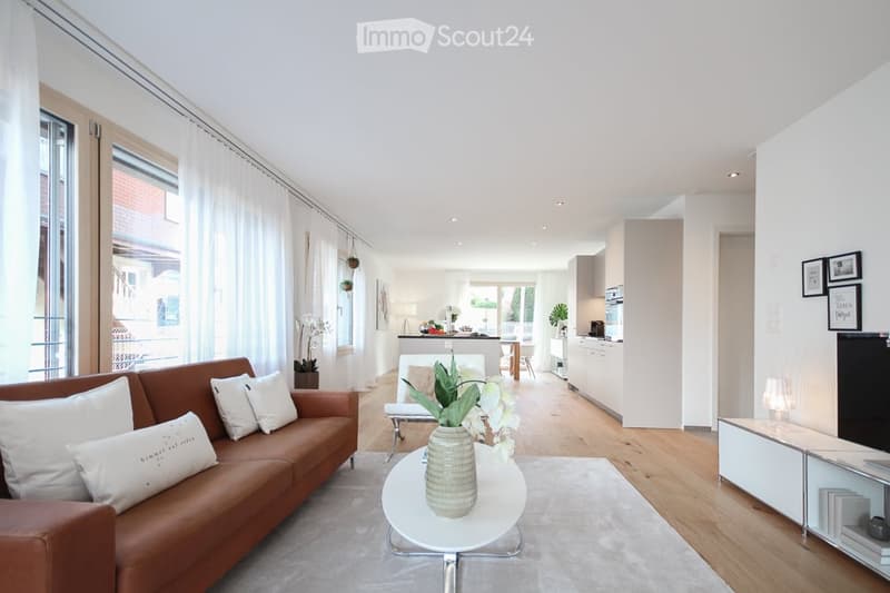 modern living room with white walls, wooden floor, large windows, brown sofa, white coffee table, white rug, white cabinets, kitchen area, TV