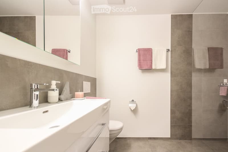 modern bathroom with white sink, mirror, shower, toilet, towel rack, and tiled walls