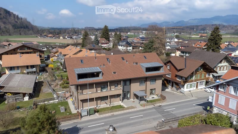 Aerial view of a residential area with several houses, brown roofs, solar panels, and a road.