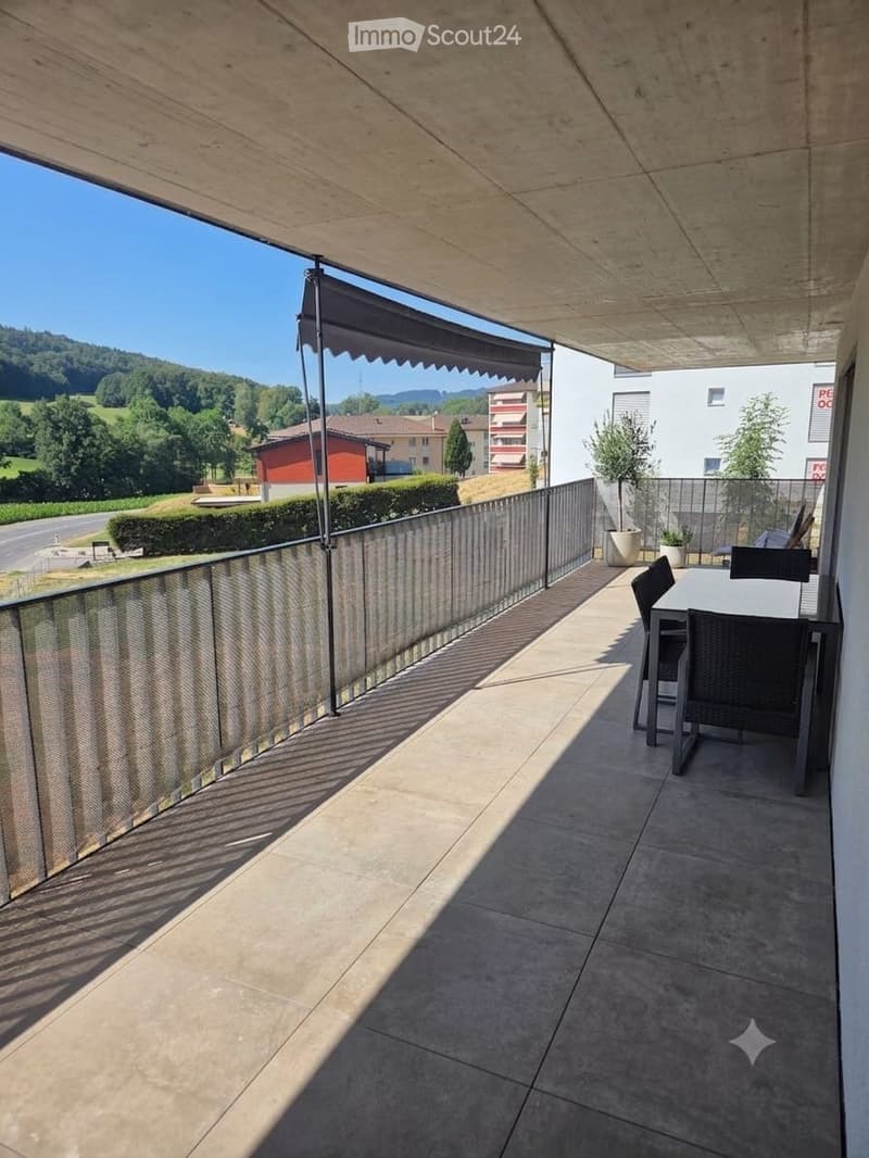 Balcony with a table and chairs, modern railing, and a view of a green landscape.
